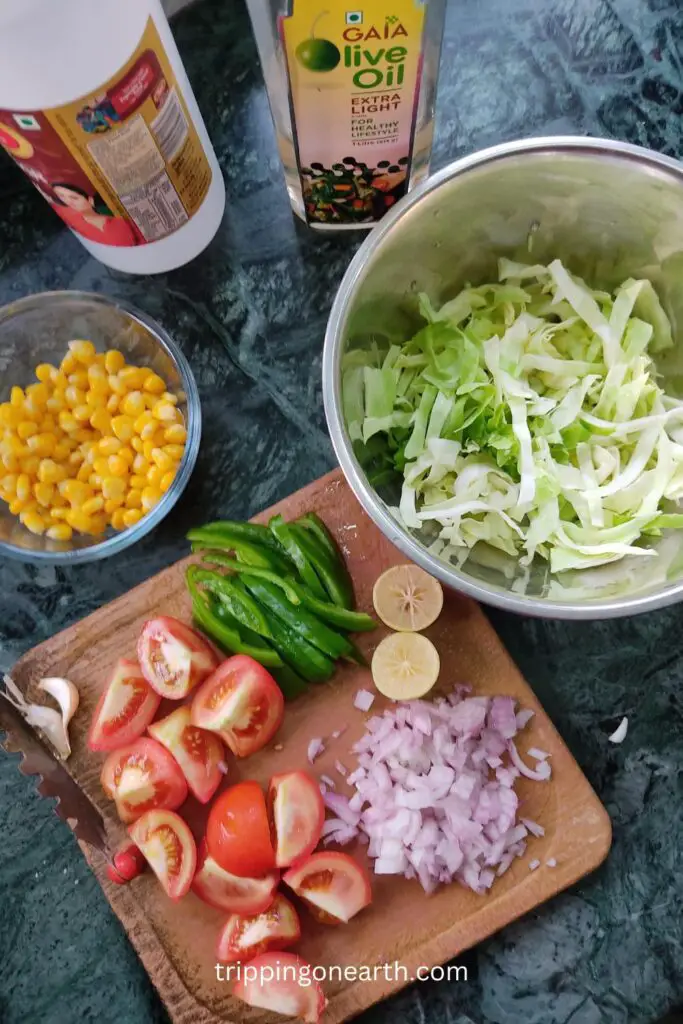 halved lemons, quartered tomatoes, chopped onions, and capsicum, sweet corn,  on a chopping board. and chopped cabbage in separate bowls