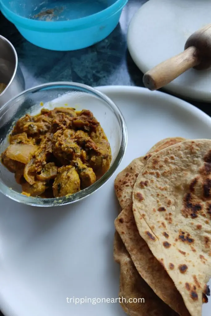 mushroom do pyaza in a glass bowl along with parathas on a white plate