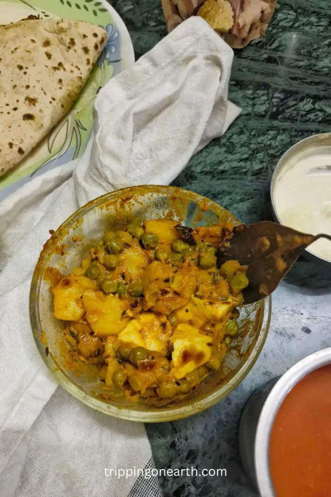 aloo matar paneer in a glass bowl with fresh cream. flatbreads, tomato puree, and white cloth in the background