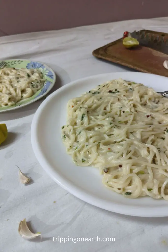 creamy lemon garlic pasta on a plate and lemon, garlic and knife cloves on the table