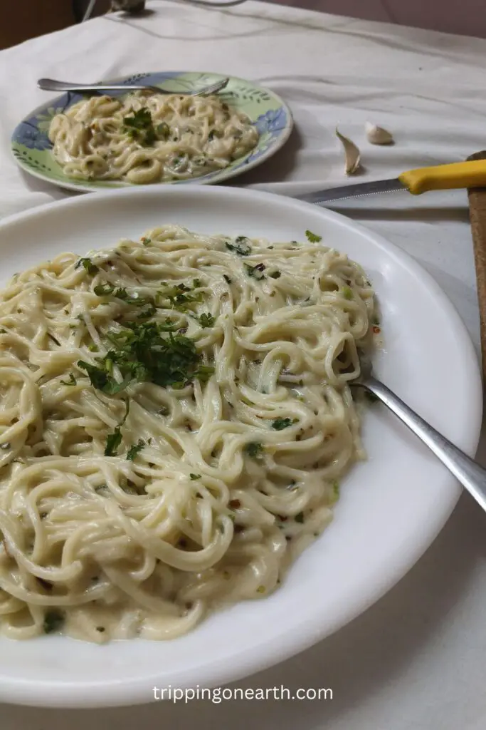 creamy lemon garlic pasta on a plate, garnished with coriander leaves, and lemon, garlic and knife cloves on the table beside it