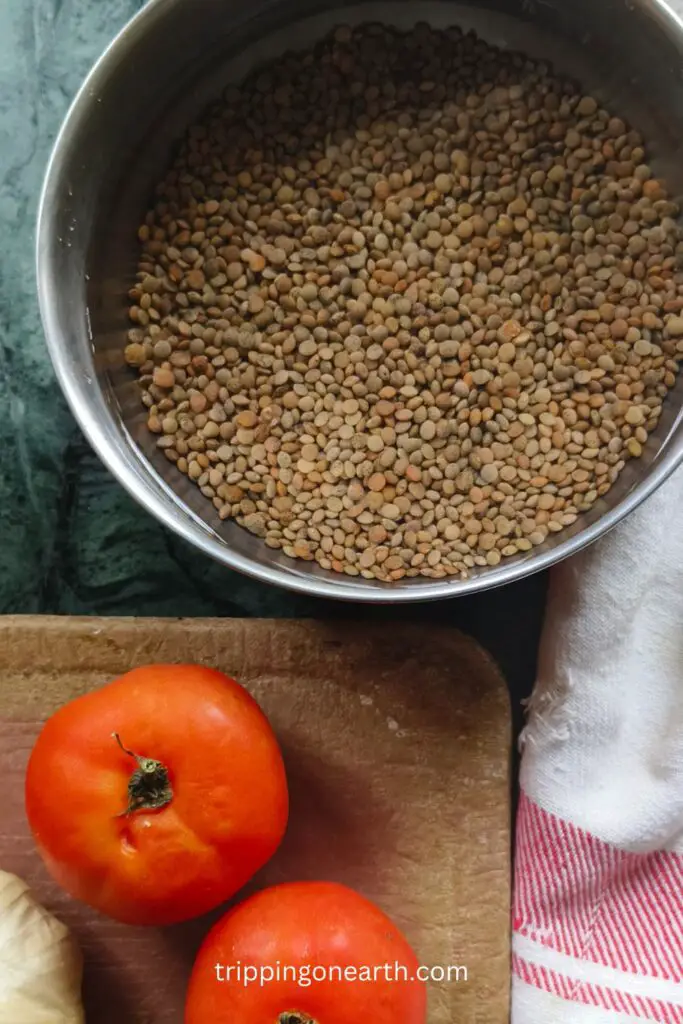 raw kali masoor dal in a bowl, and tomatoes and a white cloth beside it