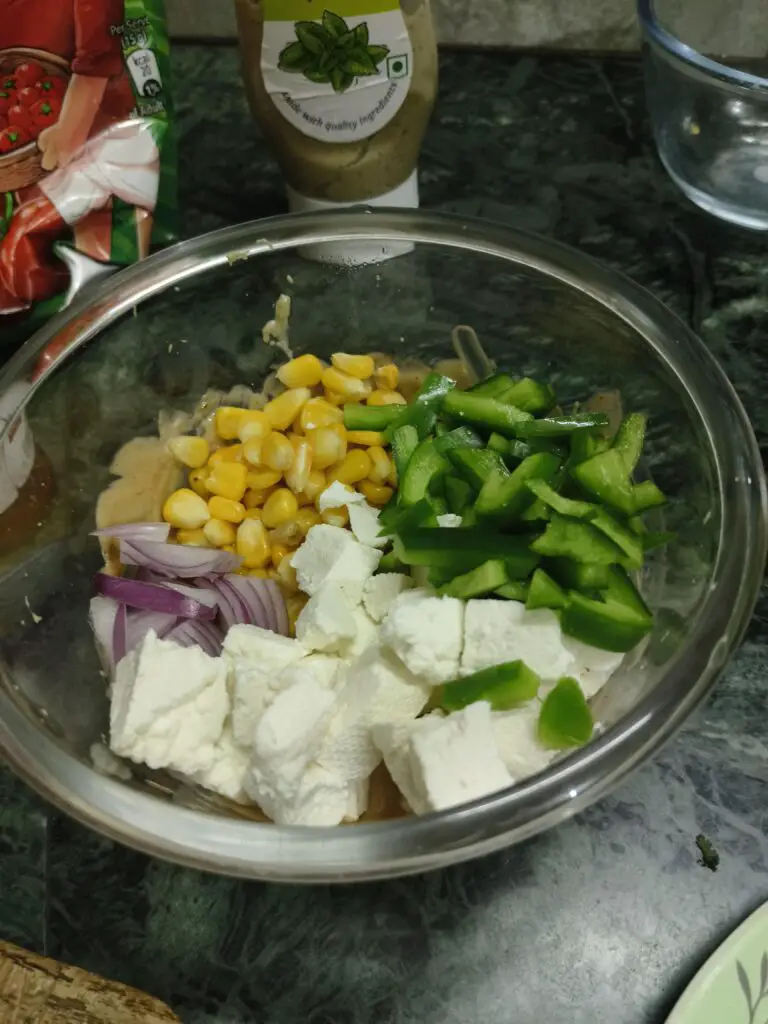 paneer, onion, capsicum, and sweet corn kernels on top of the sauce in the bowl