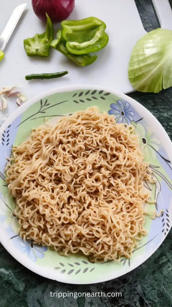 boiled millet noodles on a plate, and uncut vegetables beside it on a white chopping board