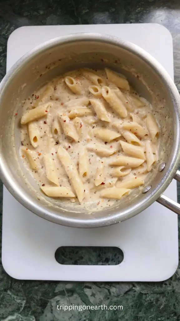 penne pasta with alfredo sauce in a skillet on top of a white chopping board