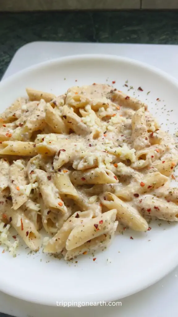 penne pasta with alfredo sauce on a white plate on top of a white chopping board
