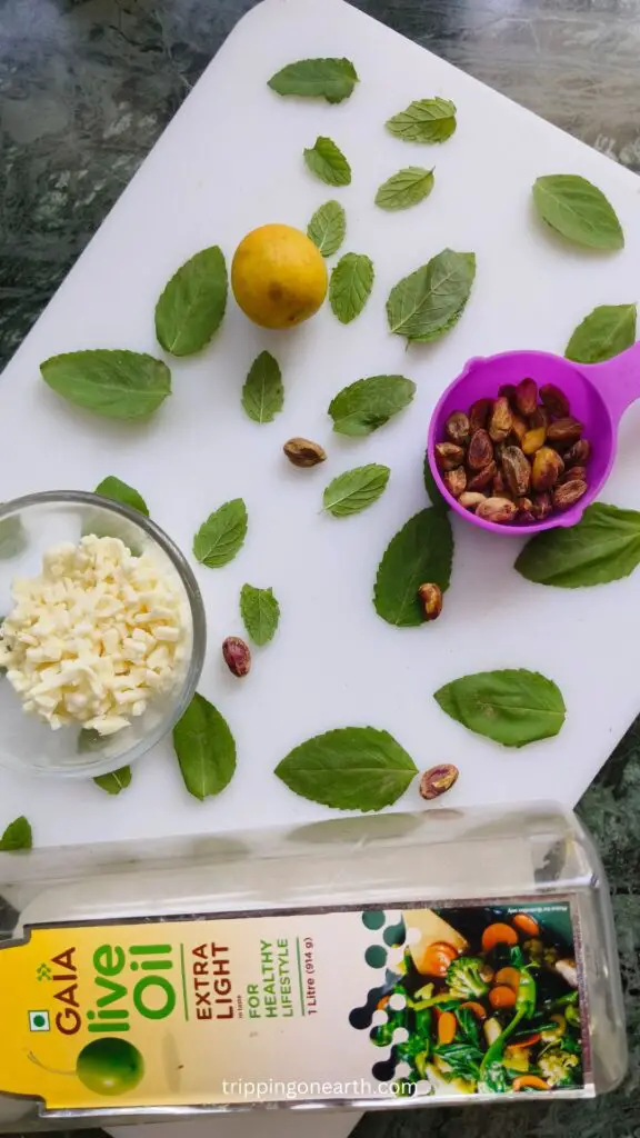 ingredients laid out on a white board- cheese, basil, pistachios, lemon, and olive oil.