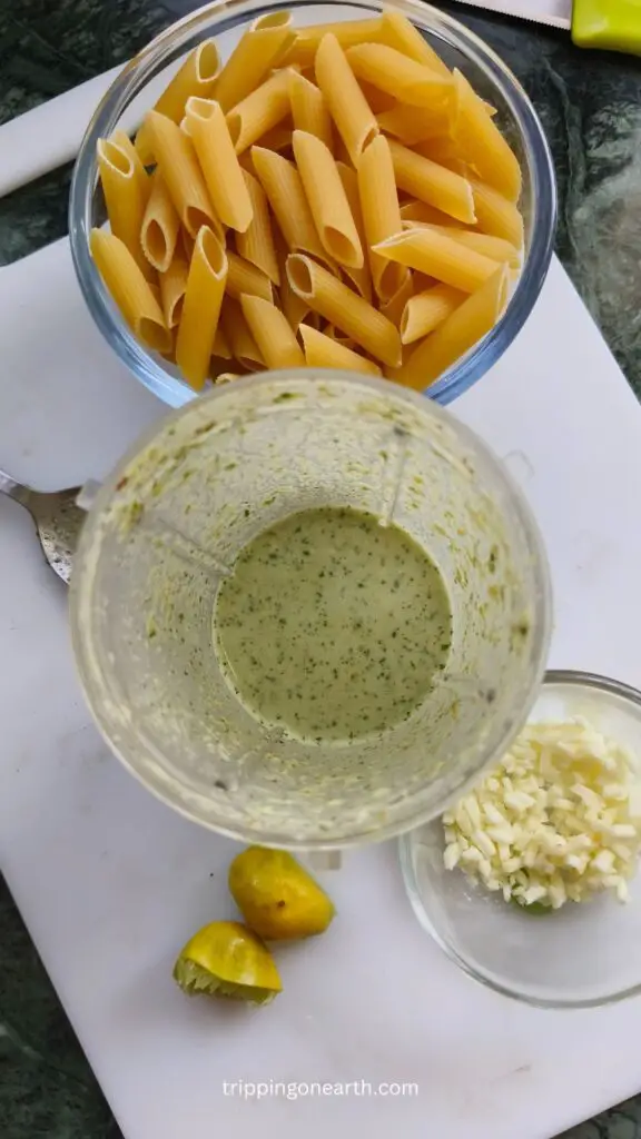 top view of pistachio sauce in a blender and cheese and raw pasta set besides it