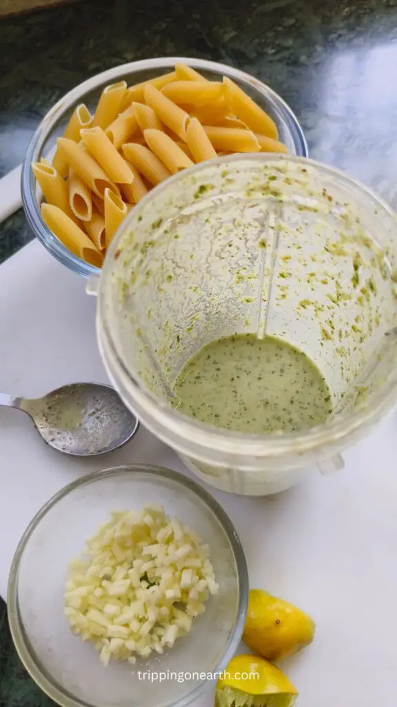 pistachio sauce in a blender and cheese and raw pasta set besides it