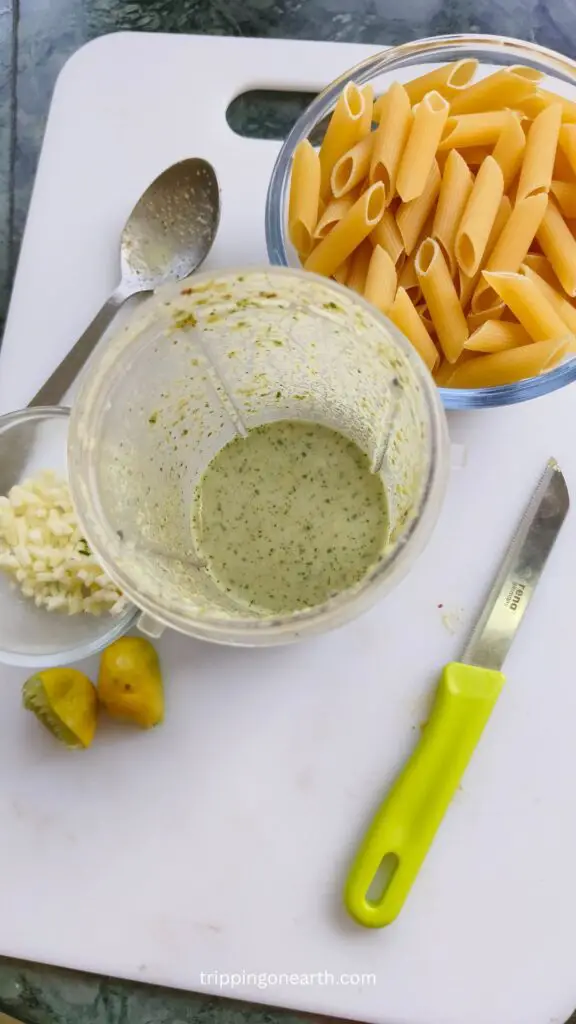 top side view pistachio sauce in a blender and cheese and raw pasta set besides it
