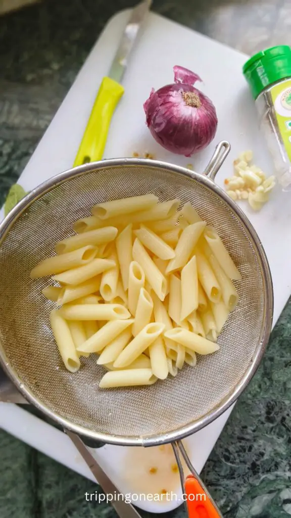 cooked penne pasta in a strainer on a white chopping board