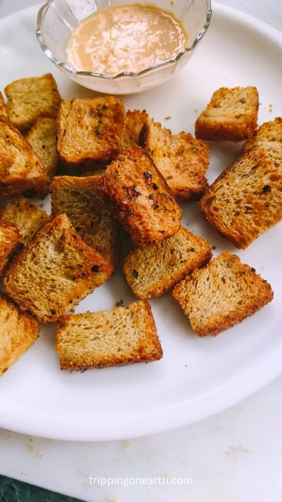 Air fryer croutons on a white plate with a dipping sauce on the side